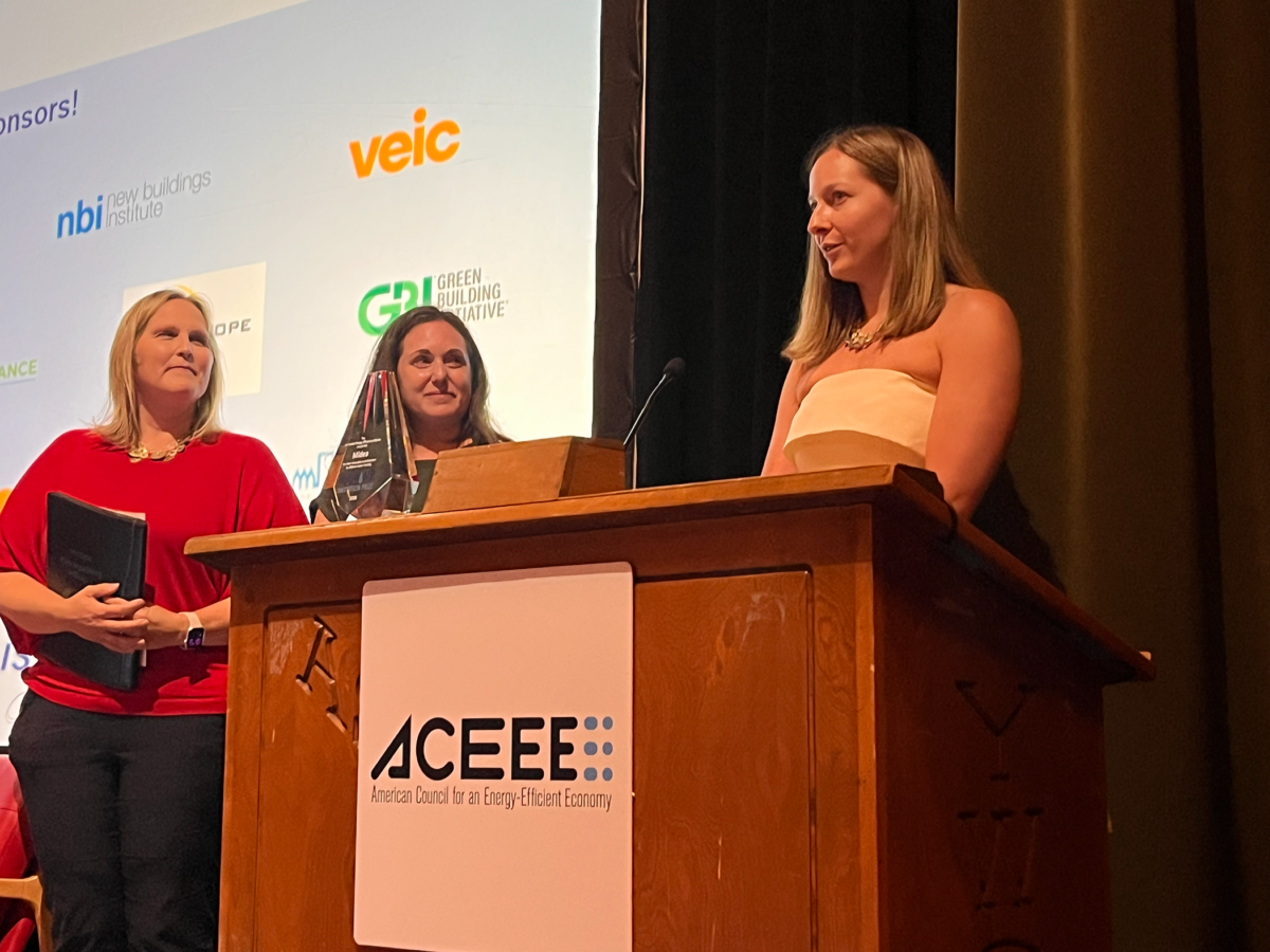 One woman speaks from a lectern while two other women watch.